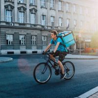 Image of a young food delivery man, riding on a bicycle in the downtown area.